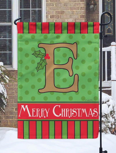 Monogram letter E Christmas burlap garden flag, 13x18 double applique, two sided, hanging on a black stand beside evergreens and holiday lights.