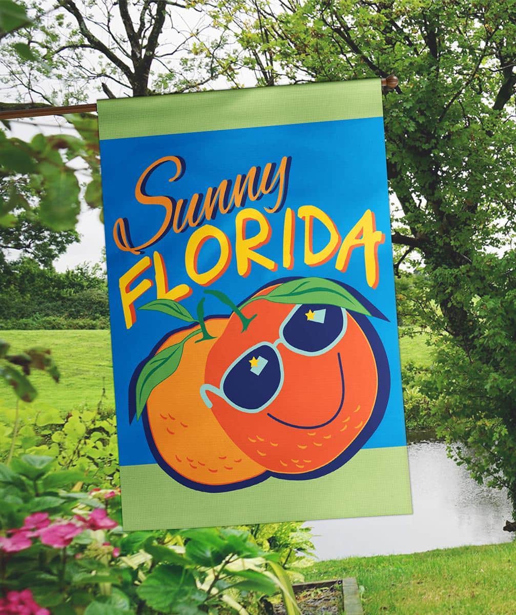 29x42 Florida Oranges Sunny double applique banner flag showing bright oranges, green leaves, and a warm sun motif on a blue background, displayed mounted on a porch pole.