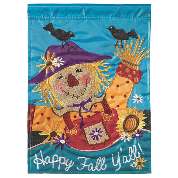 13x18 Happy Fall Yall garden flag with double applique scarecrow, pumpkins, leaves and Warm autumn lettering, shown mounted on a garden flag stand beside a front porch planter.