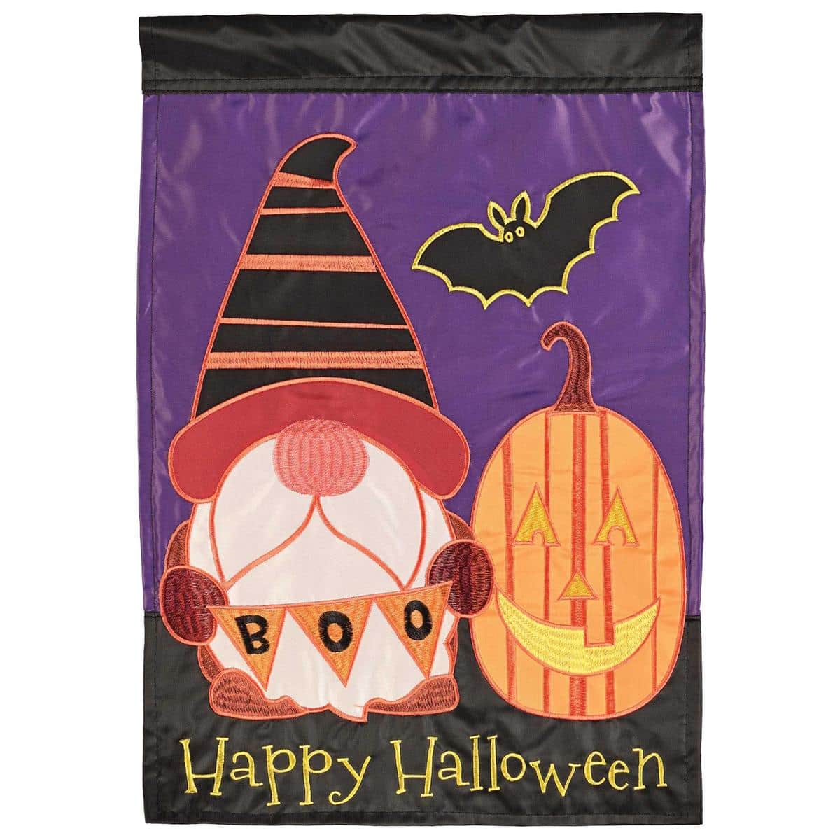 Double applique 13x18 Happy Halloween gnome garden flag with jack-o-lantern accents and bold lettering, displayed on a yard stand beside fall mums and pumpkins.