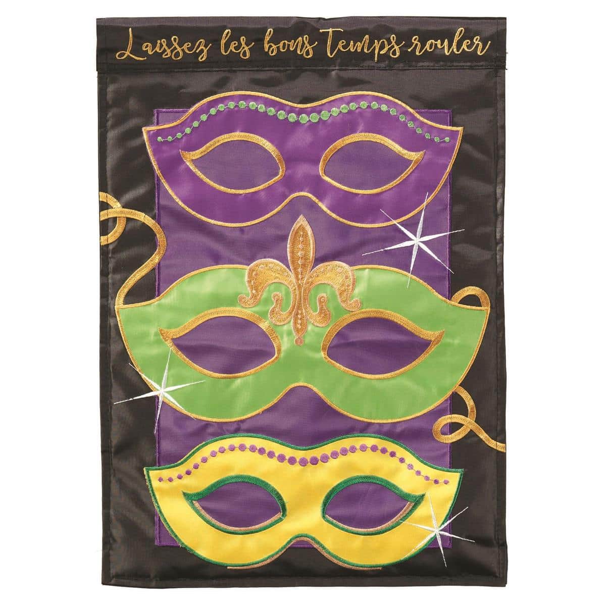 Close-up photo of a 13x18 Mardi Gras Mask garden flag with double applique purple, green, and gold mask elements, layered fabric textures, and a reinforced sleeve for a standard garden flag pole, displayed outdoors on a grassy yard near a porch.
