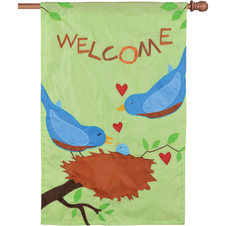 Applique Flag - Bluebirds featuring a colorful bluebird design with the word 'WELCOME' displayed outdoors in a garden setting.