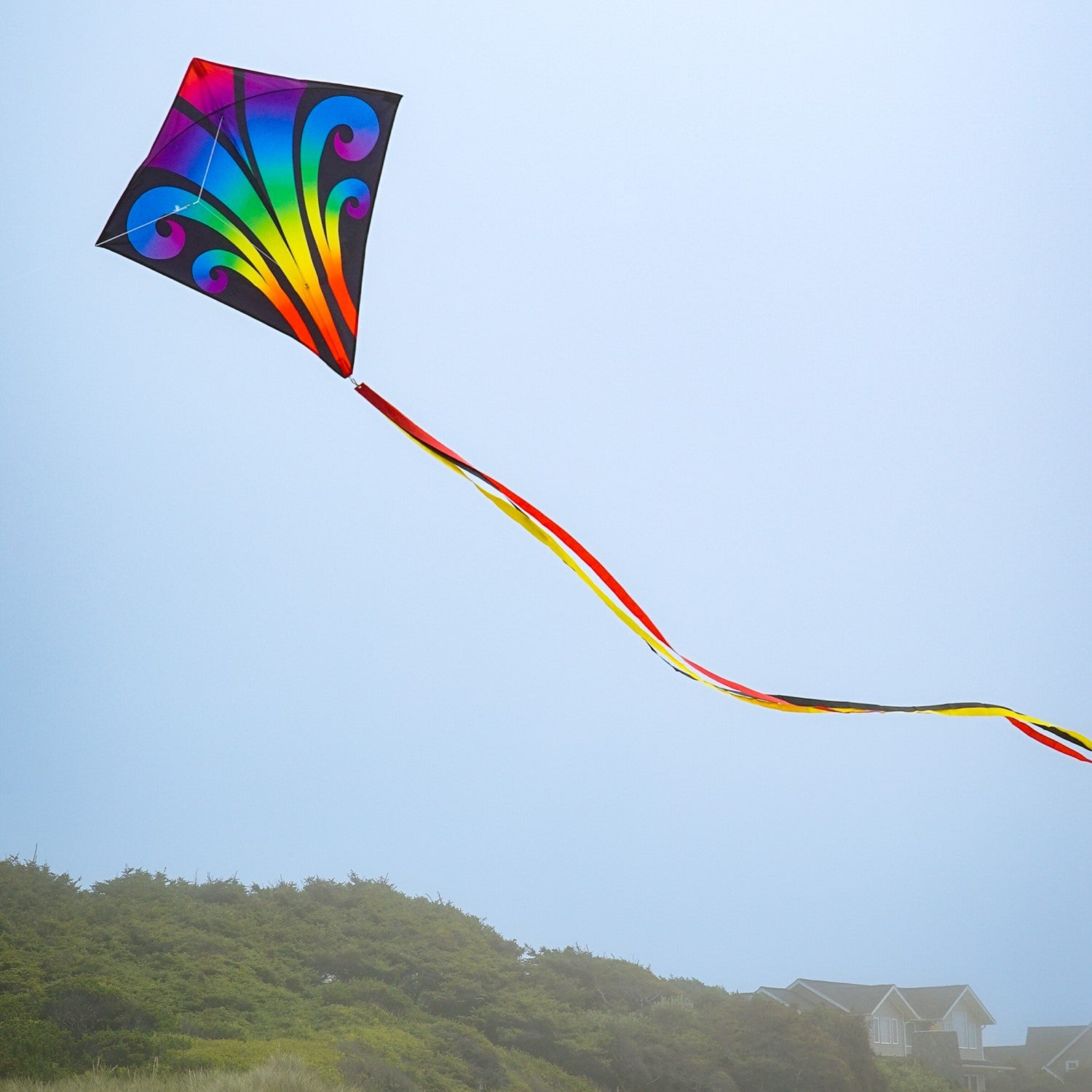 Aurora 30-inch diamond kite featuring vibrant colors and tails, soaring against a clear blue sky, captured in a fun outdoor setting.