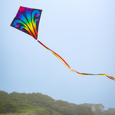 Aurora 30-inch diamond kite featuring vibrant colors and tails, soaring against a clear blue sky, captured in a fun outdoor setting.