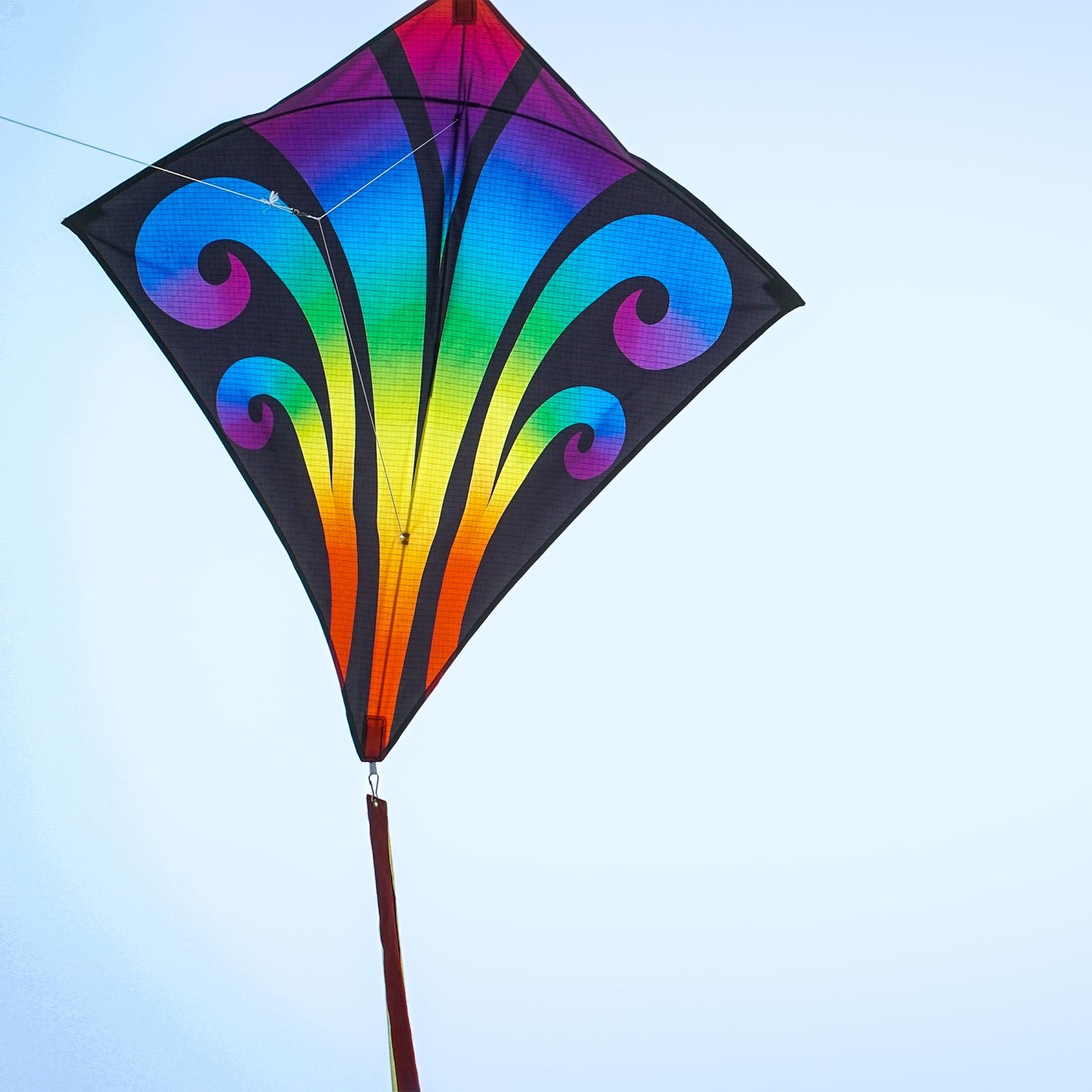 Aurora 30-inch diamond kite featuring vibrant colors and tails, soaring against a clear blue sky, captured in a fun outdoor setting.