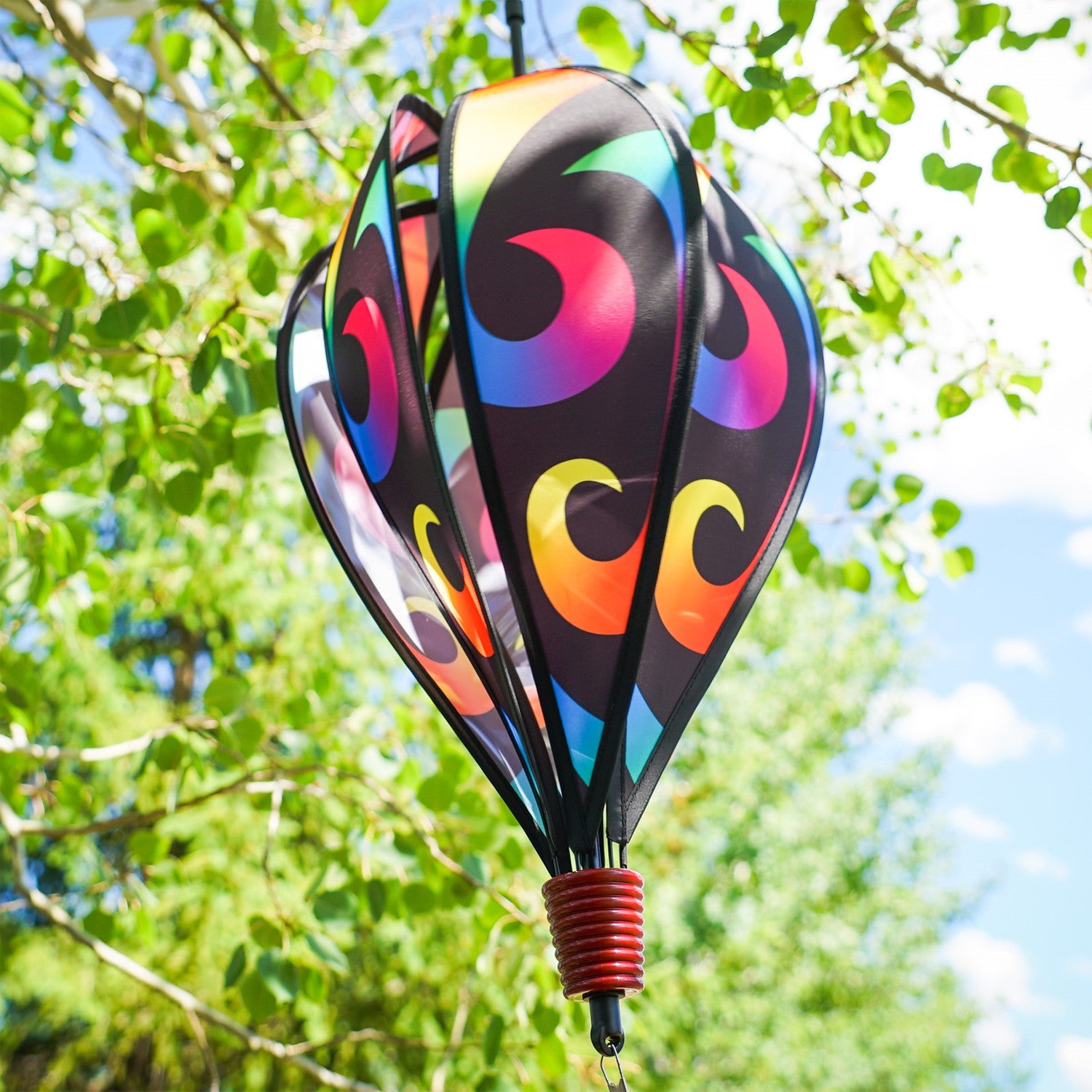Aurora 6-Panel Hot Air Balloon in vibrant rainbow colors, displayed in a garden setting, spinning gracefully with colorful tail.