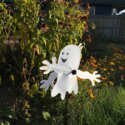 Baby Ghost Whirligig spinning in outdoor garden setting, featuring a cheerful ghost design perfect for Halloween decor.