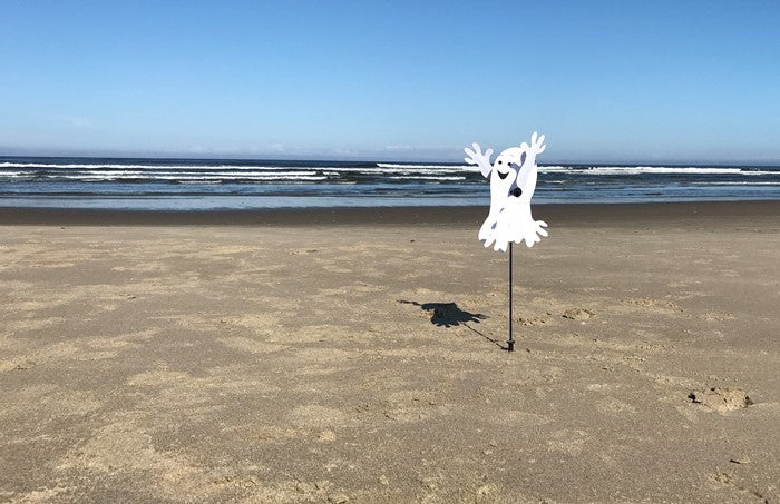 Baby Ghost Whirligig spinning in outdoor garden setting, featuring a cheerful ghost design perfect for Halloween decor.