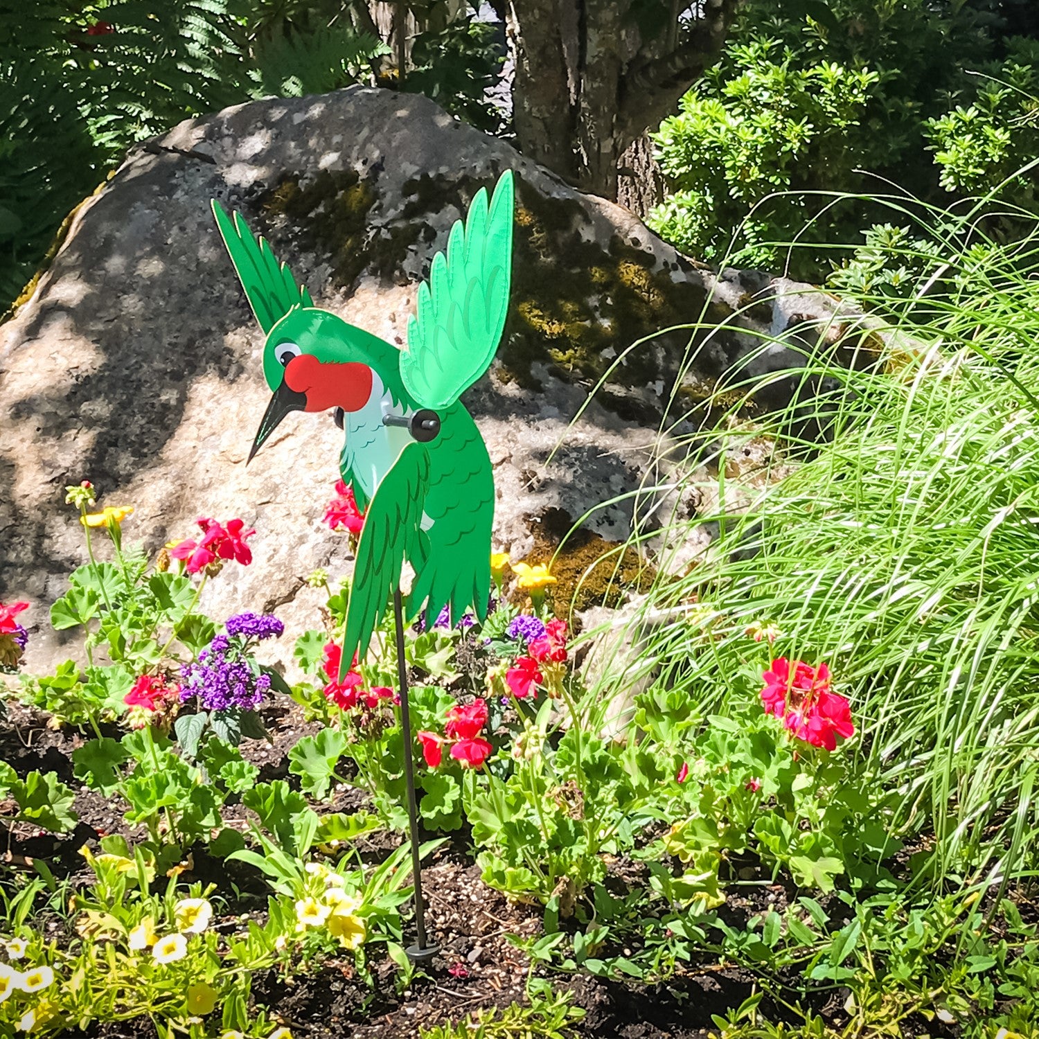Baby Hummingbird Whirligig in bright colors spins in a garden setting, showcasing its whimsical design and durable construction.