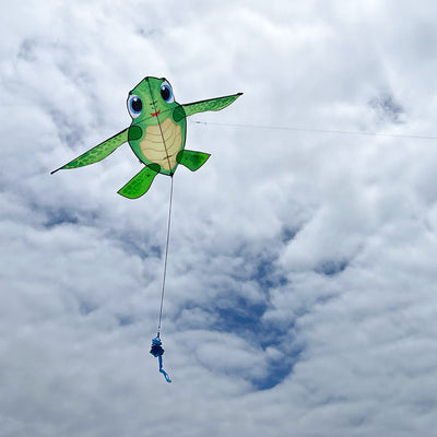 Baby Tortuga Kite featuring a cute sea turtle design and spinning tail, displayed in a clear blue sky during a sunny outdoor event.