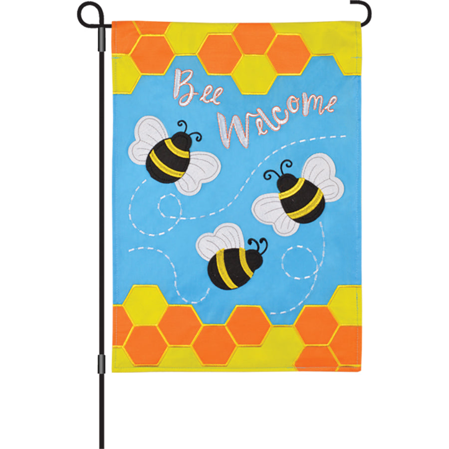 12 in. Bee Welcome garden flag with vibrant embroidered bee and floral design displayed on a garden pole in a sunny outdoor setting.