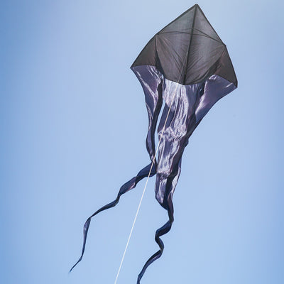 Black 77" Wave Delta Kite soaring in the sky with long flowing tails, perfect for family enjoyment and easy to fly outdoor fun.