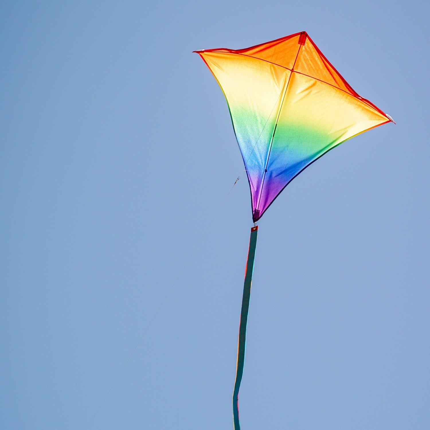 Blended Rainbow 30-inch diamond kite showcasing vibrant colors with flowing tails, soaring against a blue sky during a sunny day.