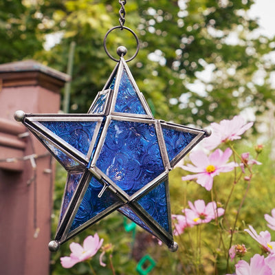 Blue 5-Point Star Hanging Tealight Lantern with textured glass panels and metal frame, suspended elegantly with a chain in an outdoor setting.