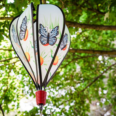 Colorful Blue Butterfly Hot Air Balloon spinner with butterfly design and daisies, displayed outdoors, showcasing movement in a garden setting.