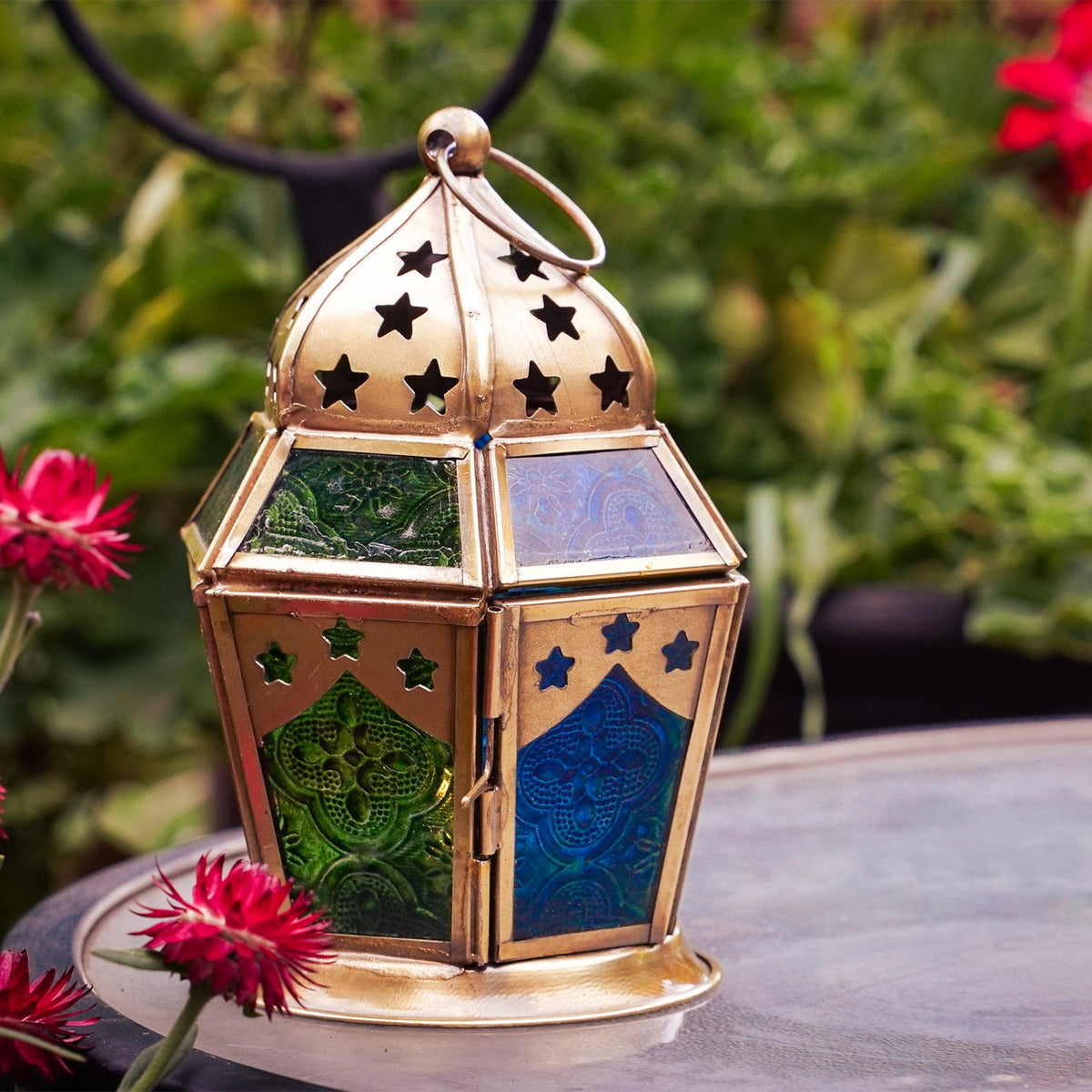 Blue & Green Hex Glass Tealight Lantern hanging in a garden, showcasing textured panels and an antiqued brass top, designed for tealight candles.