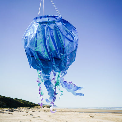 50-inch blue iridescent jellyfish 3D windsock with flowing tentacles, showcasing vibrant colors against a garden backdrop, fluttering in the wind.