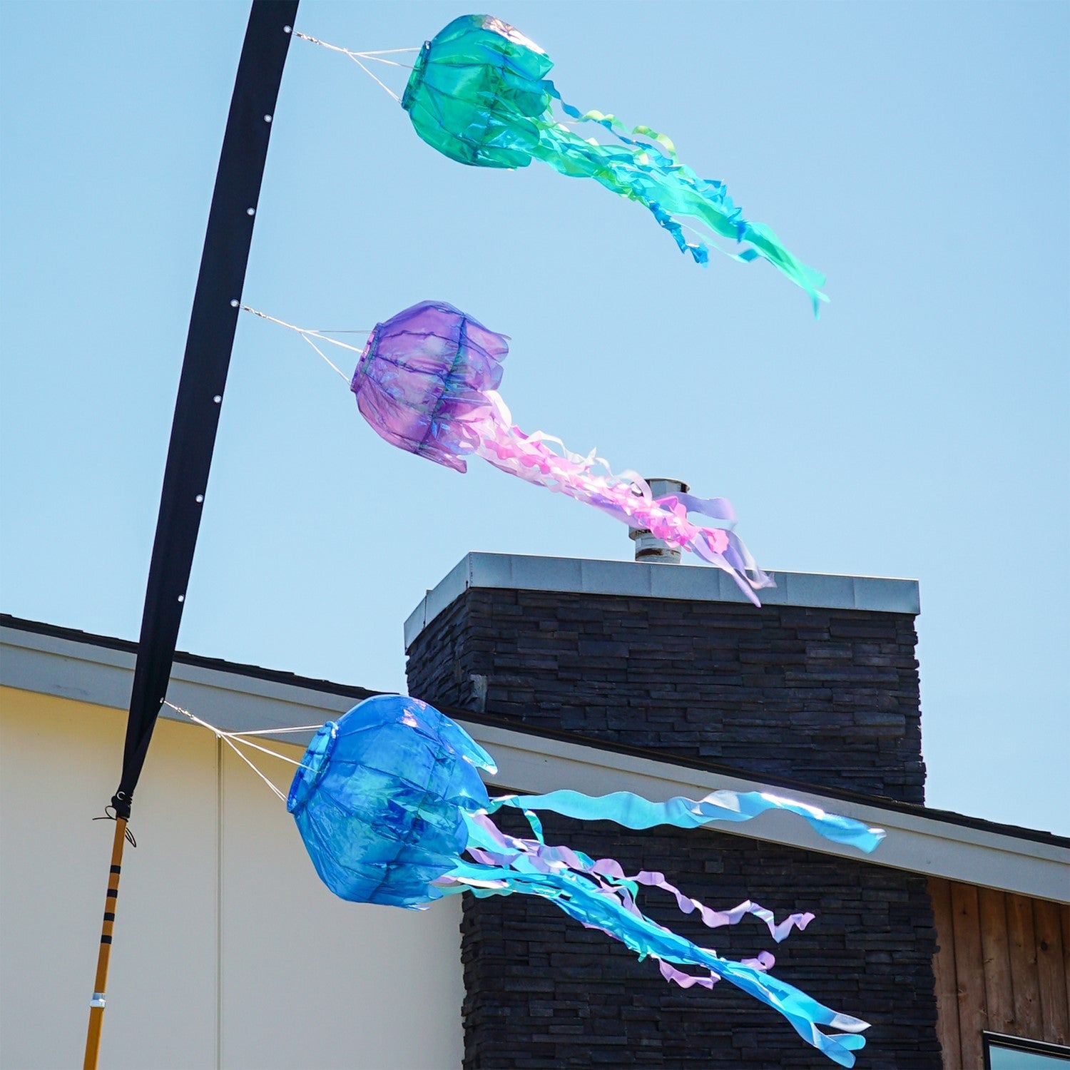 50-inch blue iridescent jellyfish 3D windsock with flowing tentacles, showcasing vibrant colors against a garden backdrop, fluttering in the wind.