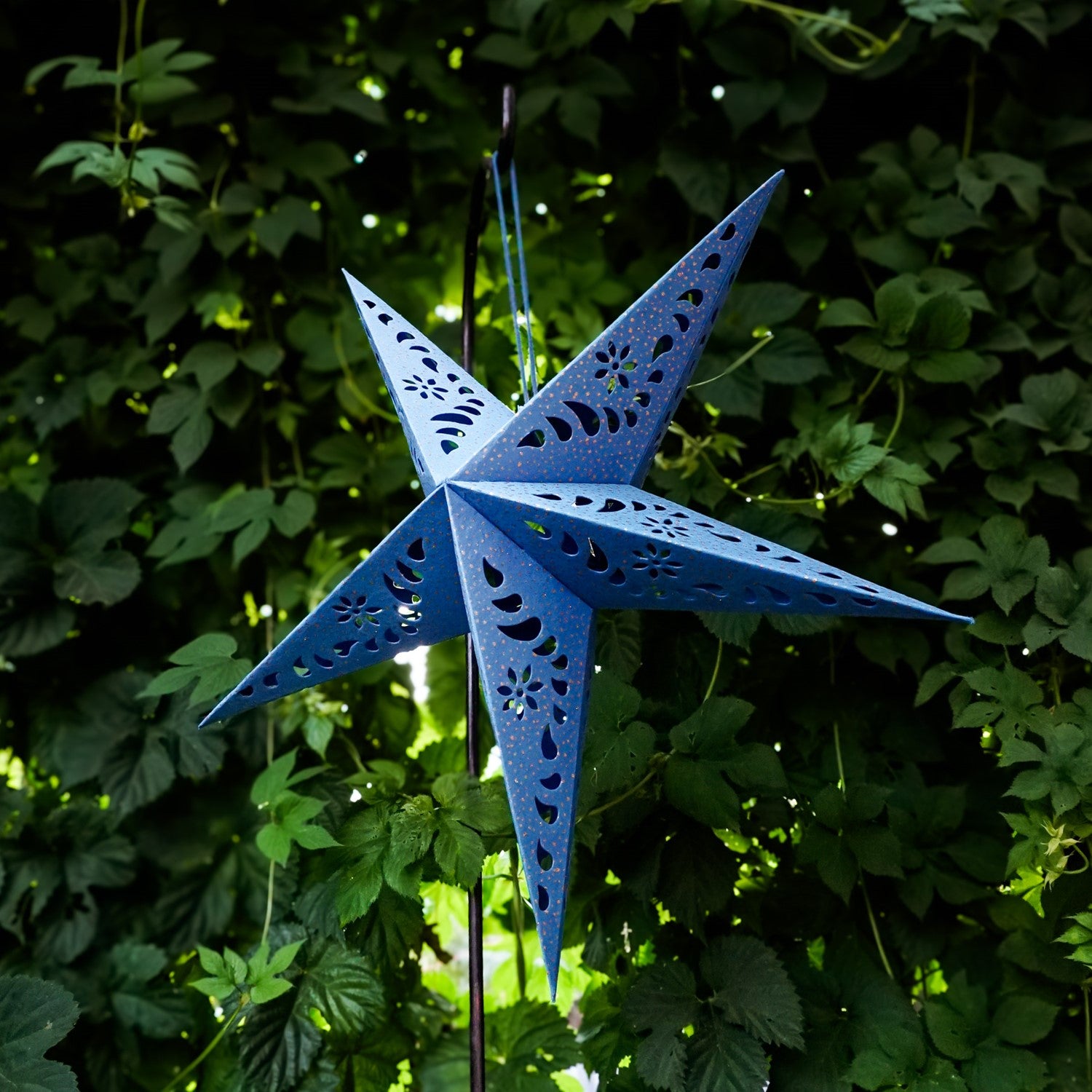 Blue Paper Star Lantern with intricate cutouts, hung indoors, providing a glowing ambiance in a boho-inspired setting.