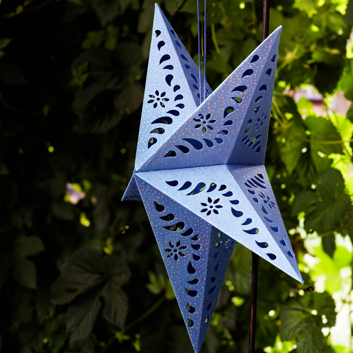Blue Paper Star Lantern with intricate cutouts, hung indoors, providing a glowing ambiance in a boho-inspired setting.