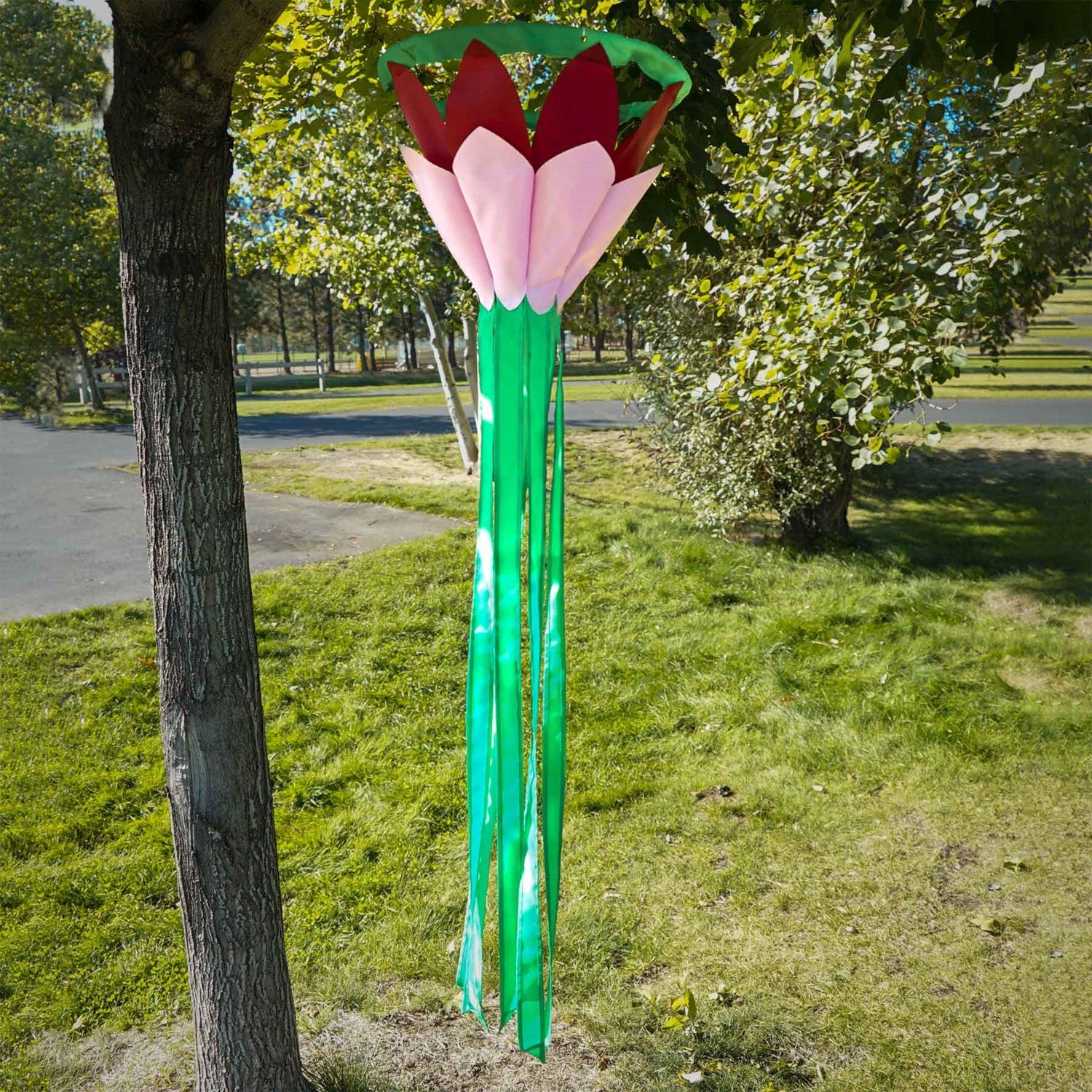 Burgundy 38' Lotus Flower Windsock with colorful petals and flowing green tails swaying gently in the breeze, enhancing a garden space.