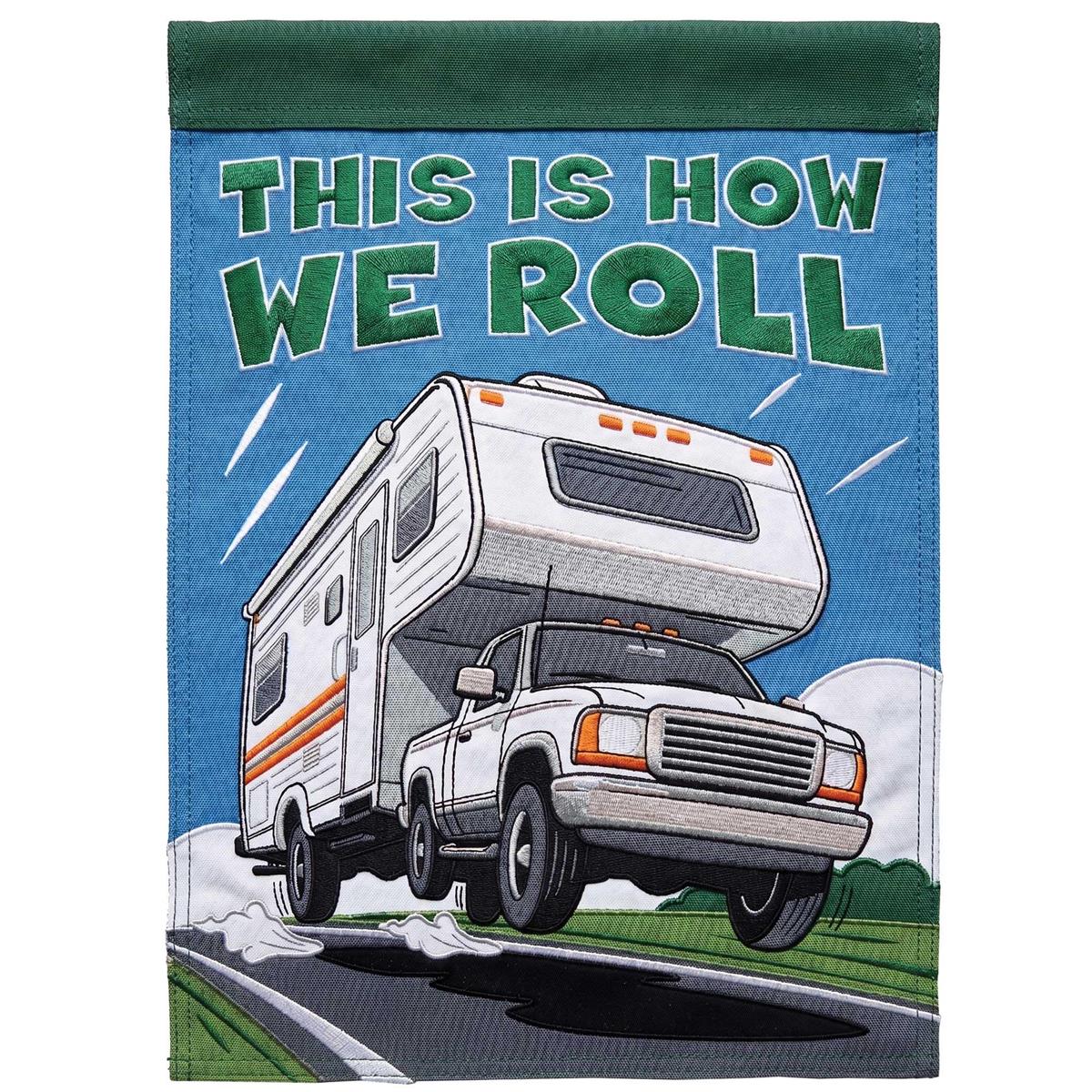 Camper This Is How We Roll garden flag, featuring vibrant colors and detailed appliques, displayed outdoors in a garden setting.