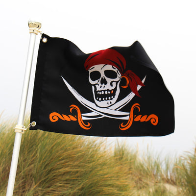 Captain Cutlass Lustre 12x18 Grommet Flag featuring a bold Jolly Roger design, displayed outdoors on a pole in a vibrant garden setting.