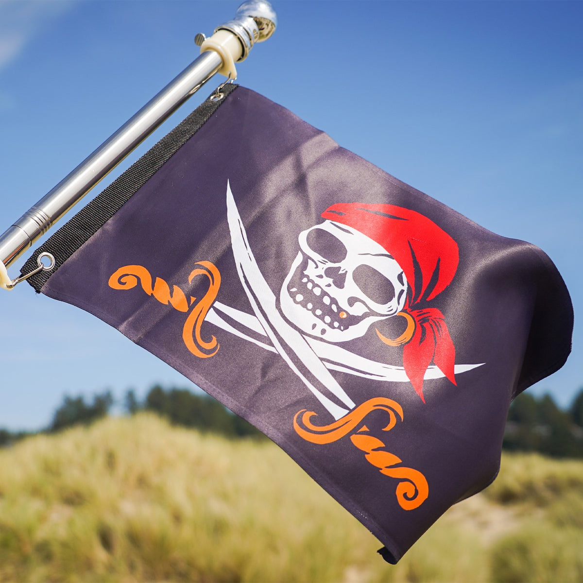Captain Cutlass Lustre 12x18 Grommet Flag featuring a bold Jolly Roger design, displayed outdoors on a pole in a vibrant garden setting.