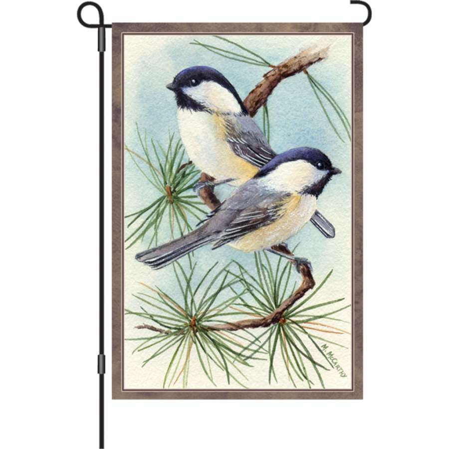 12 in. Chickadee Vignette garden flag featuring colorful chickadees and flowers displayed in a lush garden setting, illuminated for visibility.