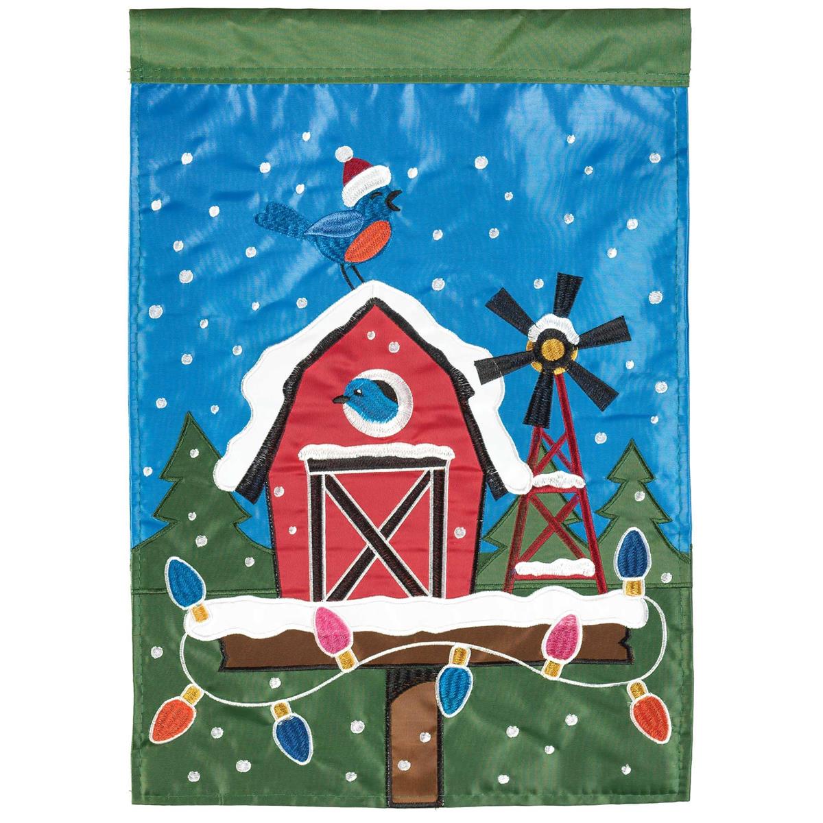 Christmas Barn Birdhouse Garden Flag featuring intricate fabric appliques and embroidery, displayed in a vibrant outdoor garden setting.