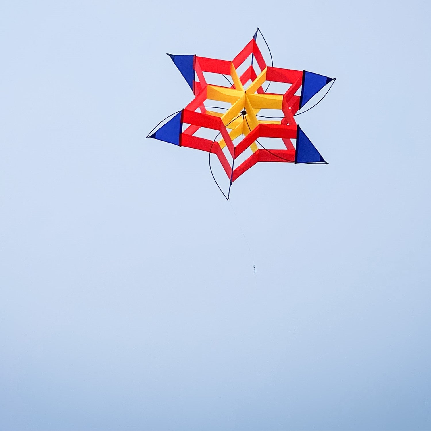Circus Cosmic Hex Kite in bright colors soaring through a blue sky with clouds, showcasing its unique hexagonal design.