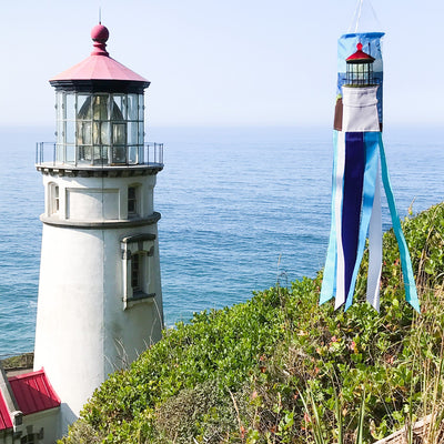 Coastal Lighthouse 40-inch windsock with vibrant lighthouse design and tails hanging elegantly from a garden in a coastal setting.