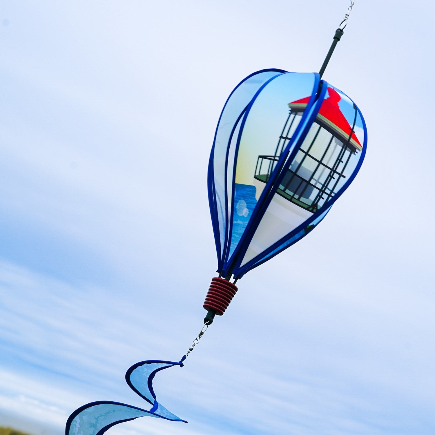 Coastal Lighthouse 6-Panel Hot Air Balloon spinner in vibrant colors with a lighthouse design hanging in a garden setting, spinning in the breeze.