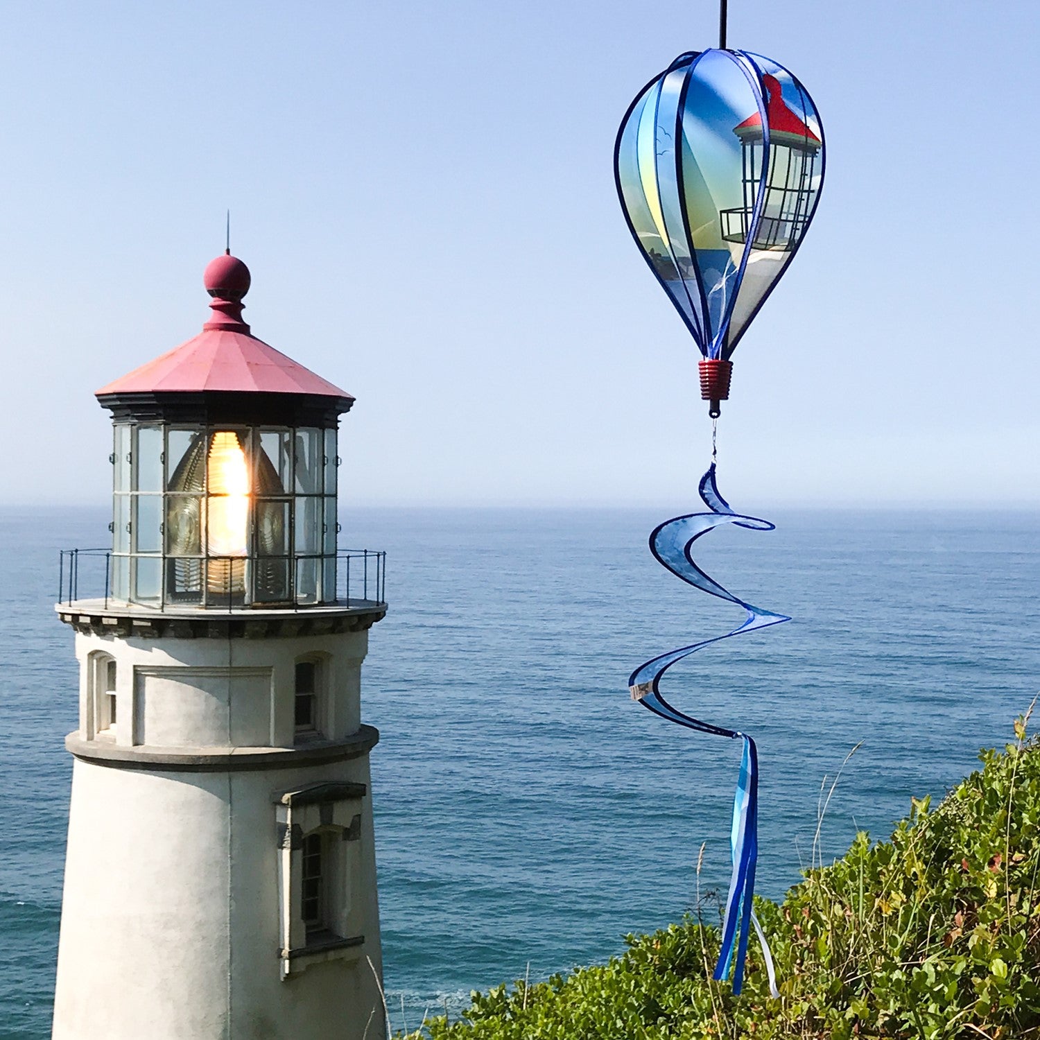 Coastal Lighthouse 6-Panel Hot Air Balloon spinner in vibrant colors with a lighthouse design hanging in a garden setting, spinning in the breeze.