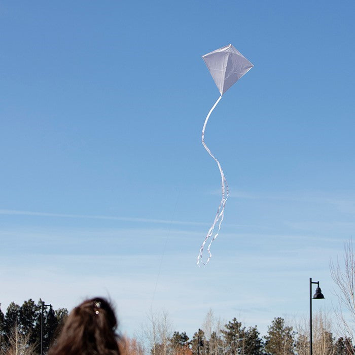 Coconut Colorfly 30-inch diamond kite in solid white color with colorful tails displayed against a clear blue sky on a sunny day.