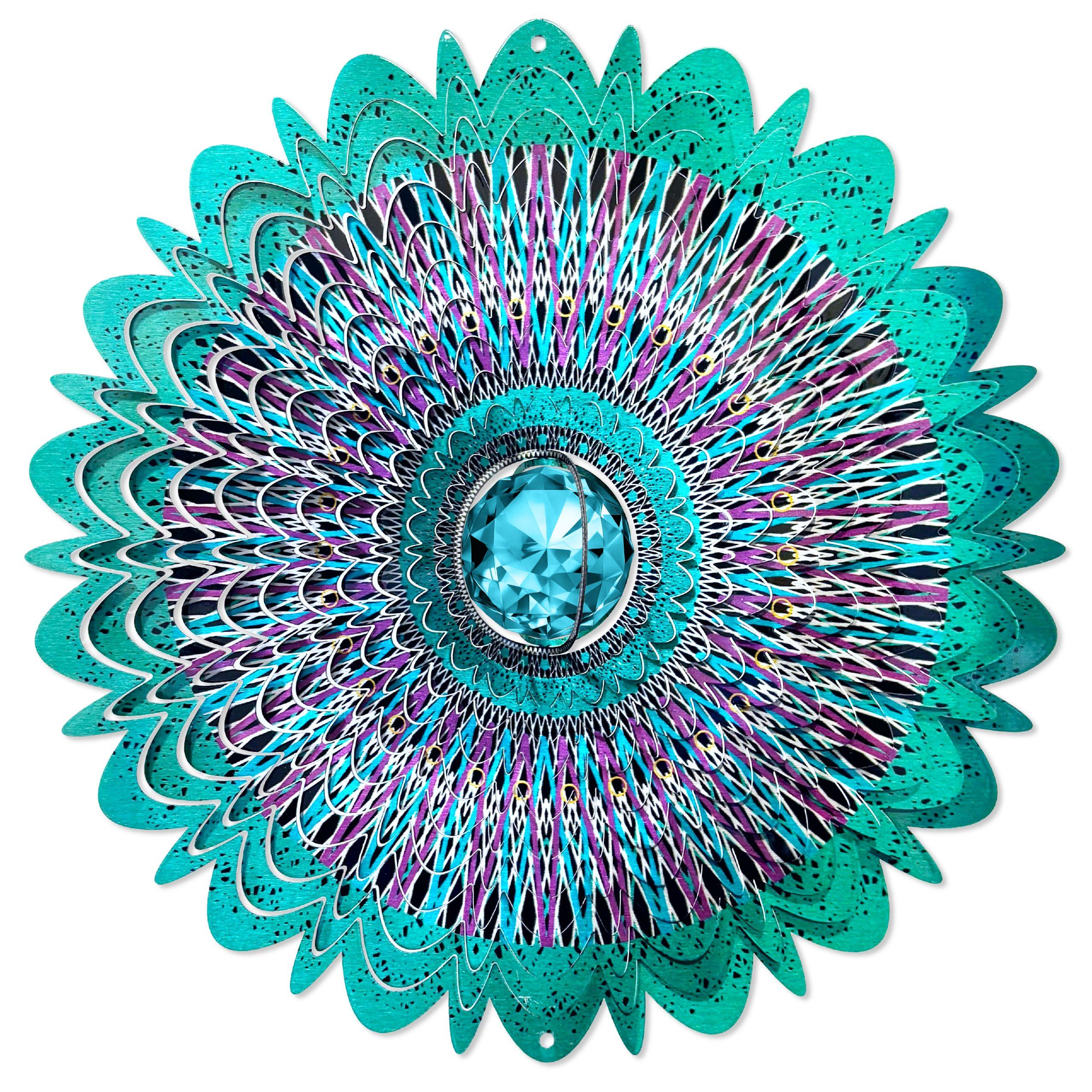 Crystal Cosmic Mandala wind spinner with a sparkling crystal centerpiece displayed in an outdoor garden setting, creating colorful reflections.