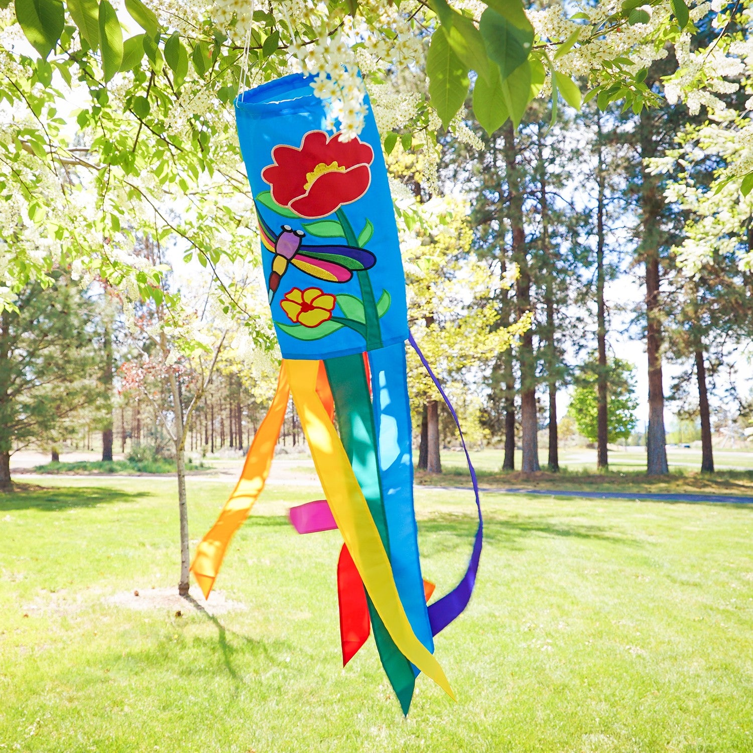 A colorful Dragonfly 40\" Windsock with appliqued graphics and fluttering tails displayed in a garden, showcasing its whimsical design.