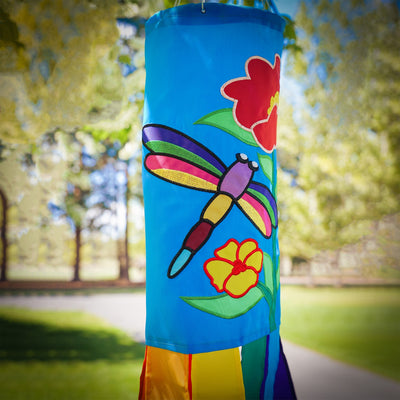 A colorful Dragonfly 40\" Windsock with appliqued graphics and fluttering tails displayed in a garden, showcasing its whimsical design.