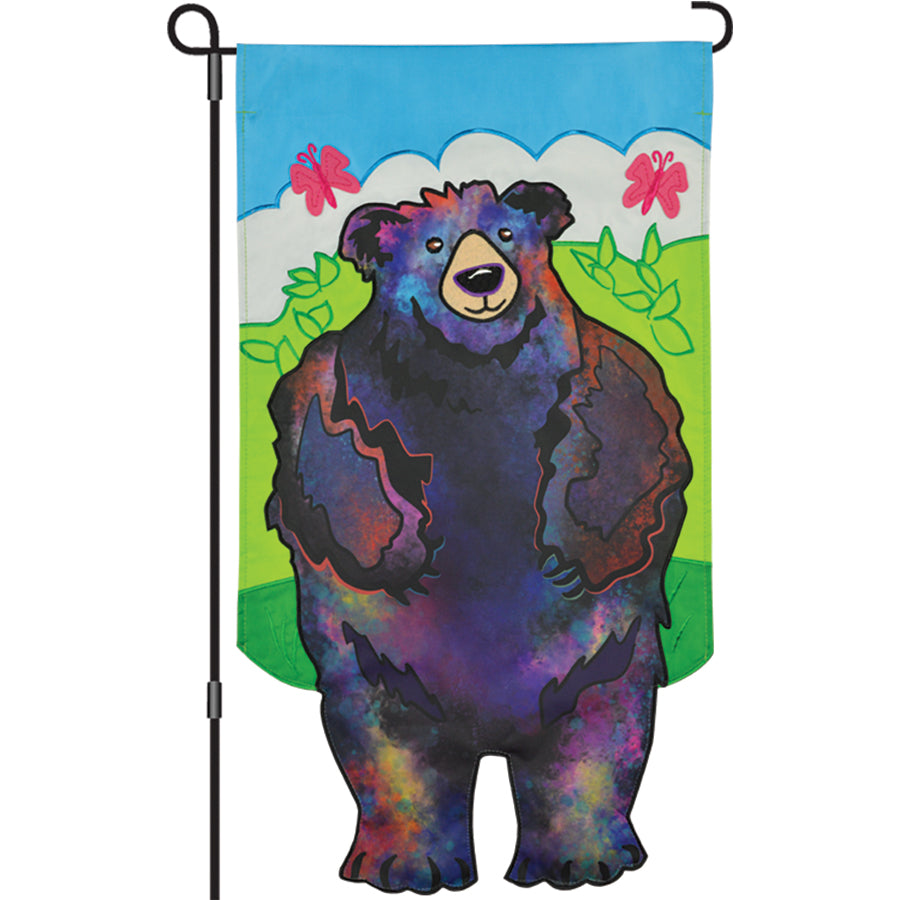 13 in. Enhanced Bear garden flag showcasing an embroidered bear design with colorful applique against a vibrant background in a garden setting.
