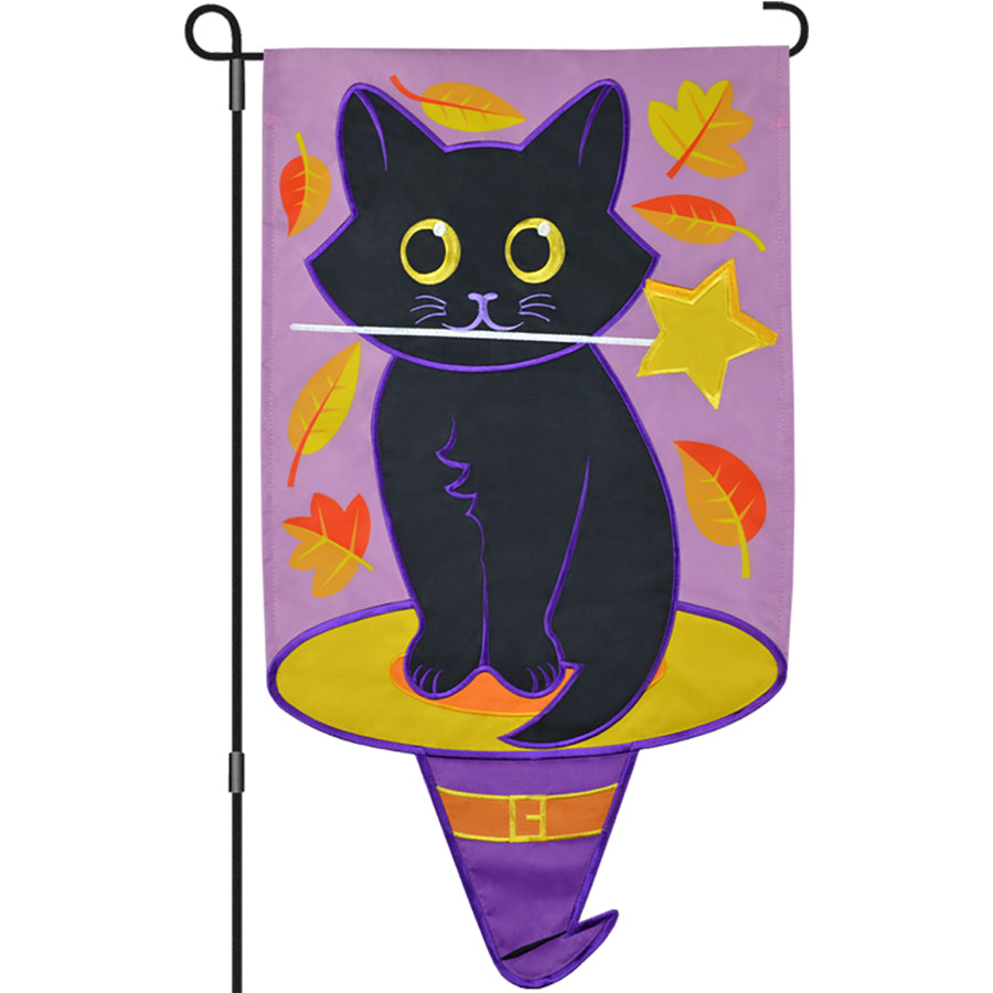 13 in. Enhanced Flag - Witch's Familiar with a whimsical black cat holding a star wand, displayed on a garden flag pole in autumn decor.