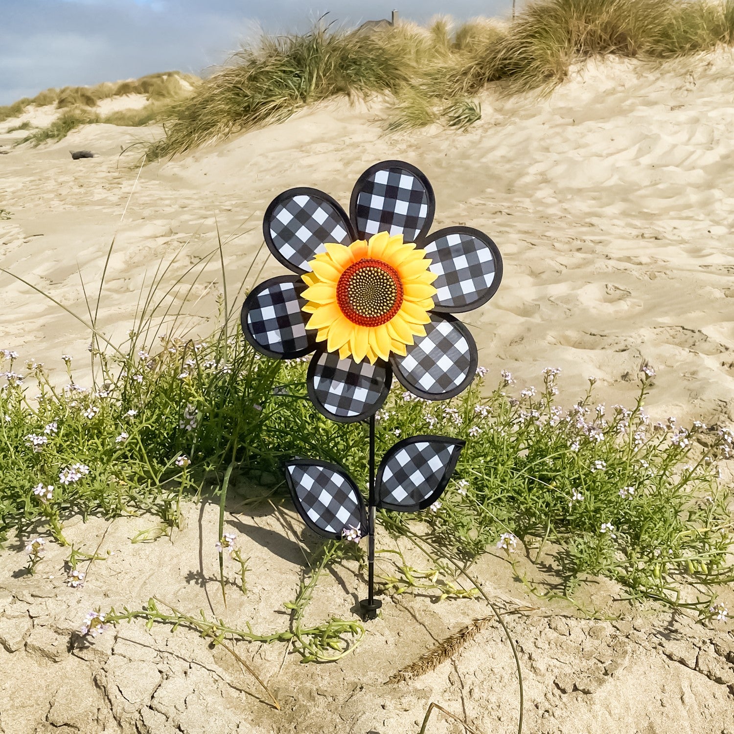 12-inch Gingham Sunflower Ground Spinner with black and white gingham petals and yellow center, spinning in a garden setting on a fiberglass pole.