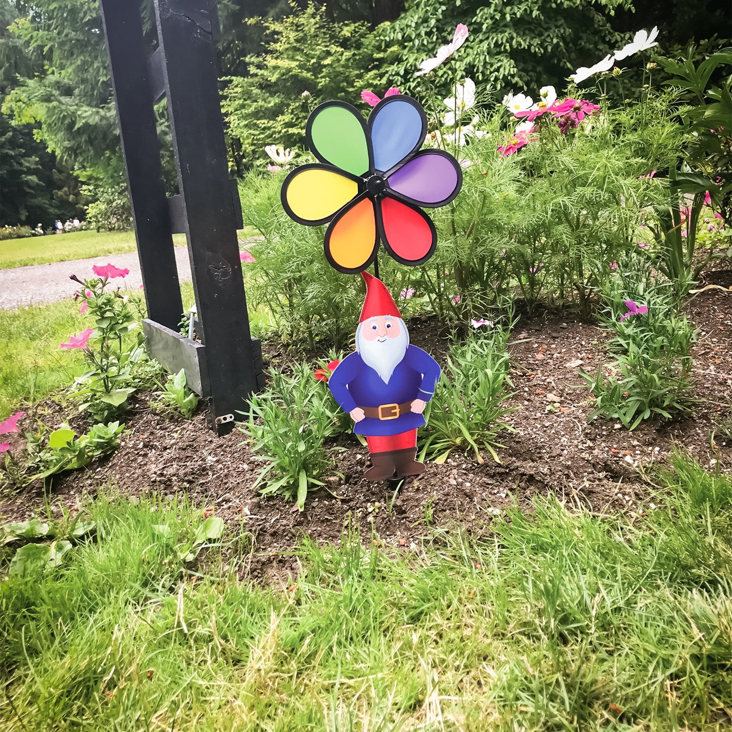 Gnome with 10-inch Rainbow Flower Spinner, featuring a whimsical design to brighten gardens, displayed outdoors with colorful motion in the breeze.