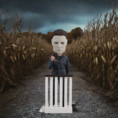Halloween Michael Myers Bobblehead leaning over a stair railing, with a ghost sheet and glasses at his feet, capturing the essence of classic horror.