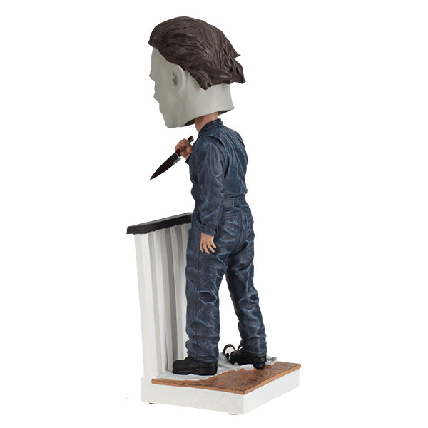 Halloween Michael Myers Bobblehead leaning over a stair railing, with a ghost sheet and glasses at his feet, capturing the essence of classic horror.