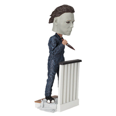 Halloween Michael Myers Bobblehead leaning over a stair railing, with a ghost sheet and glasses at his feet, capturing the essence of classic horror.