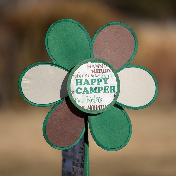 Happy Camper Flower Spinner with colorful camping flag in a garden setting, featuring a vibrant flower design and pivoting pole.