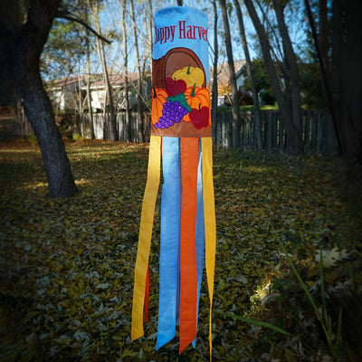 Happy Harvest 40" Windsock featuring a cornucopia design with fruits and vegetables, fluttering gracefully in a garden setting during autumn.
