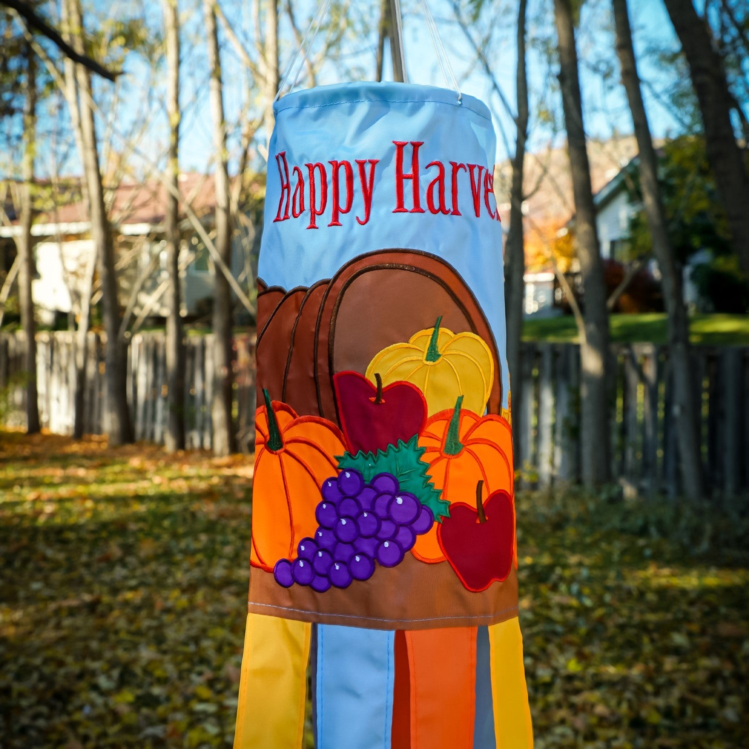 Happy Harvest 40" Windsock featuring a cornucopia design with fruits and vegetables, fluttering gracefully in a garden setting during autumn.