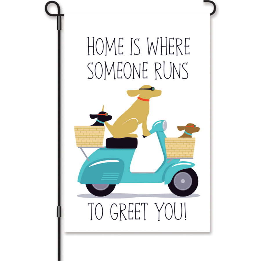 Home Is Where Someone Runs to Greet You! garden flag showcasing three dogs on a scooter, displayed in an outdoor garden setting.