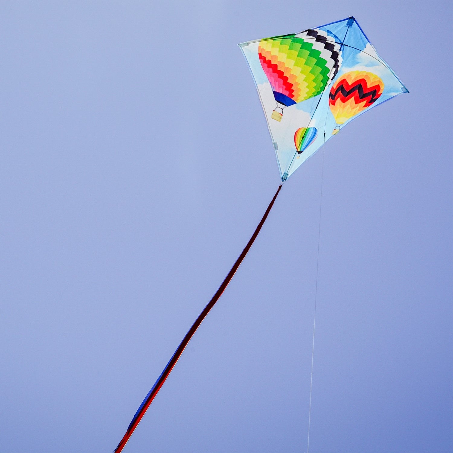 Hot Air Balloon 30" Diamond Kite with colorful design flying in a blue sky, showing vibrant colors and tails against a sunny backdrop.